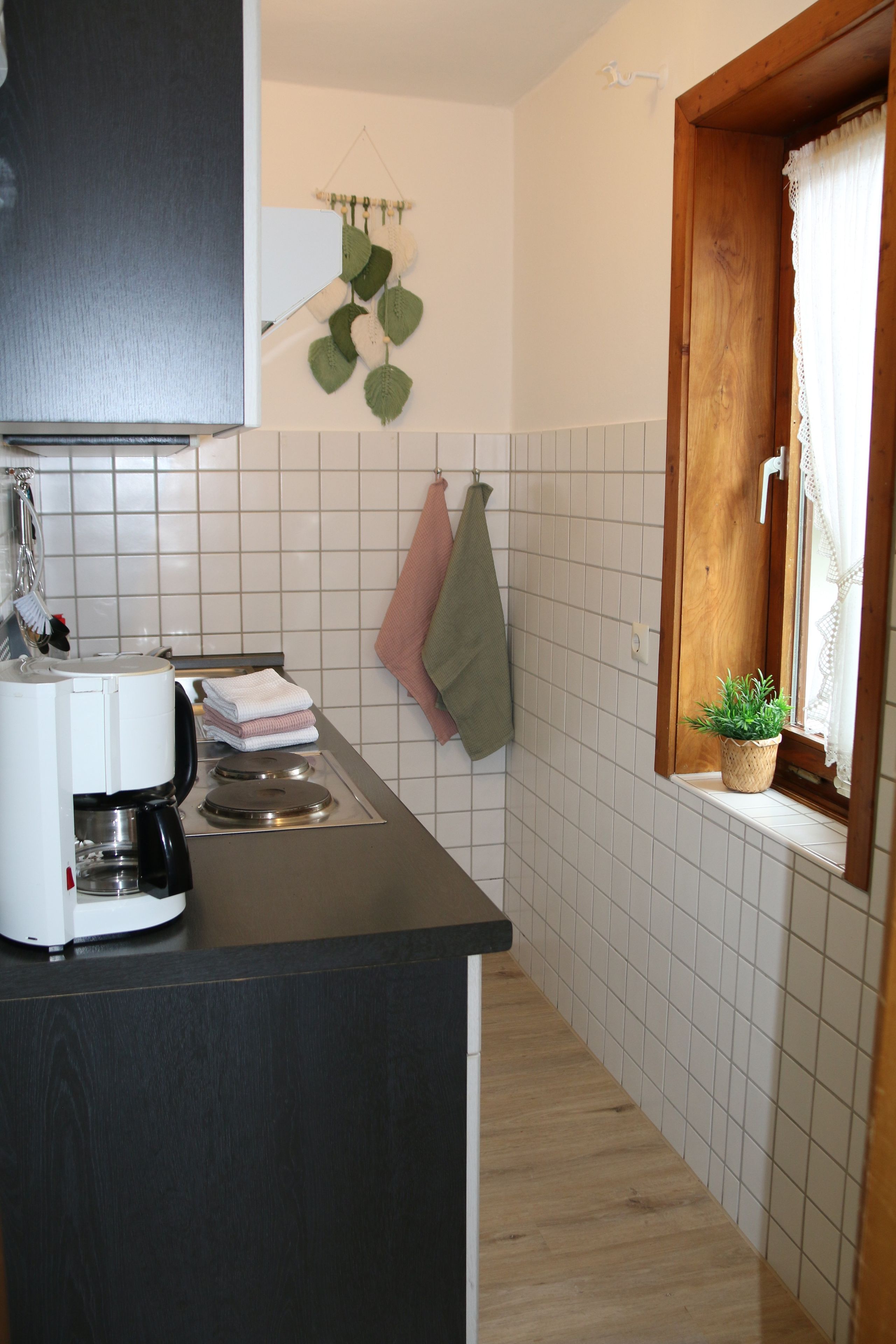 A compact kitchen with a coffee maker, a sink, and a window with a plant.