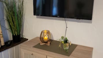 A television mounted on a wall, a wooden cabinet with drawers, a potted plant, and a candle holder with a lit candle.