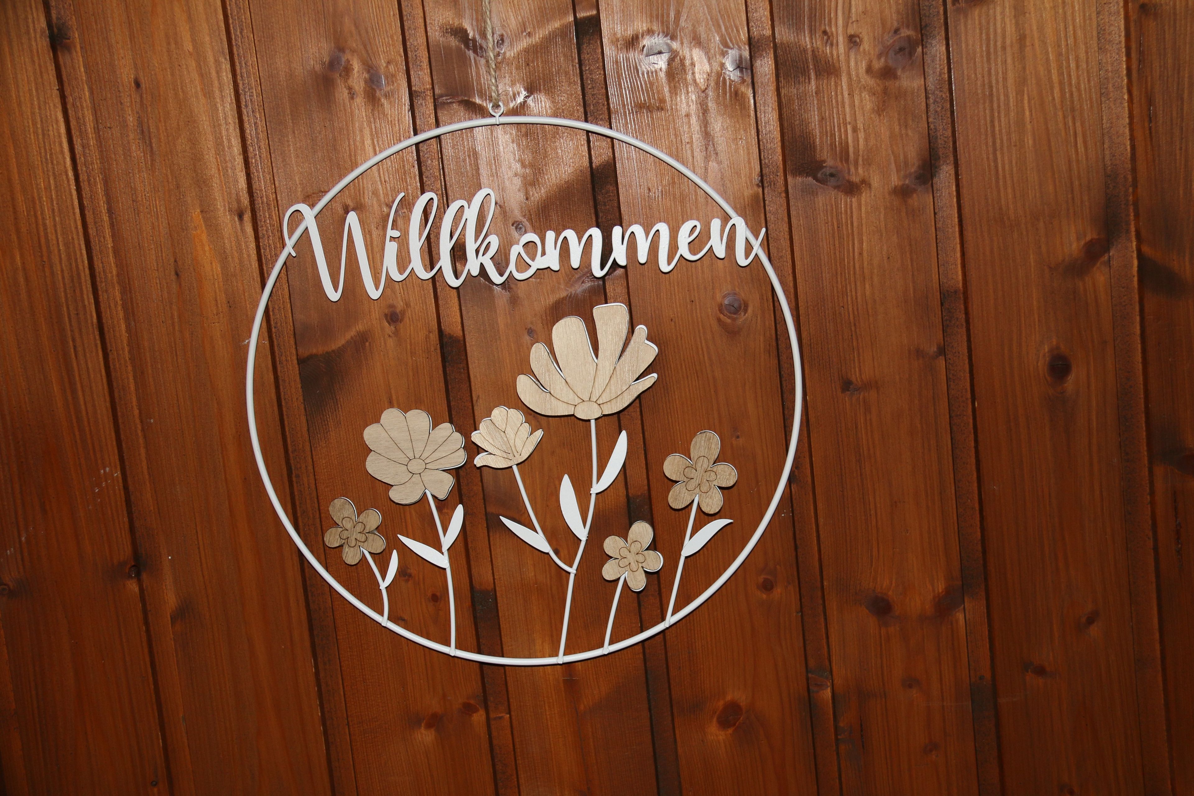 A wooden wall with a circular cut-out featuring the word 'Willkommen' and floral decorations.
