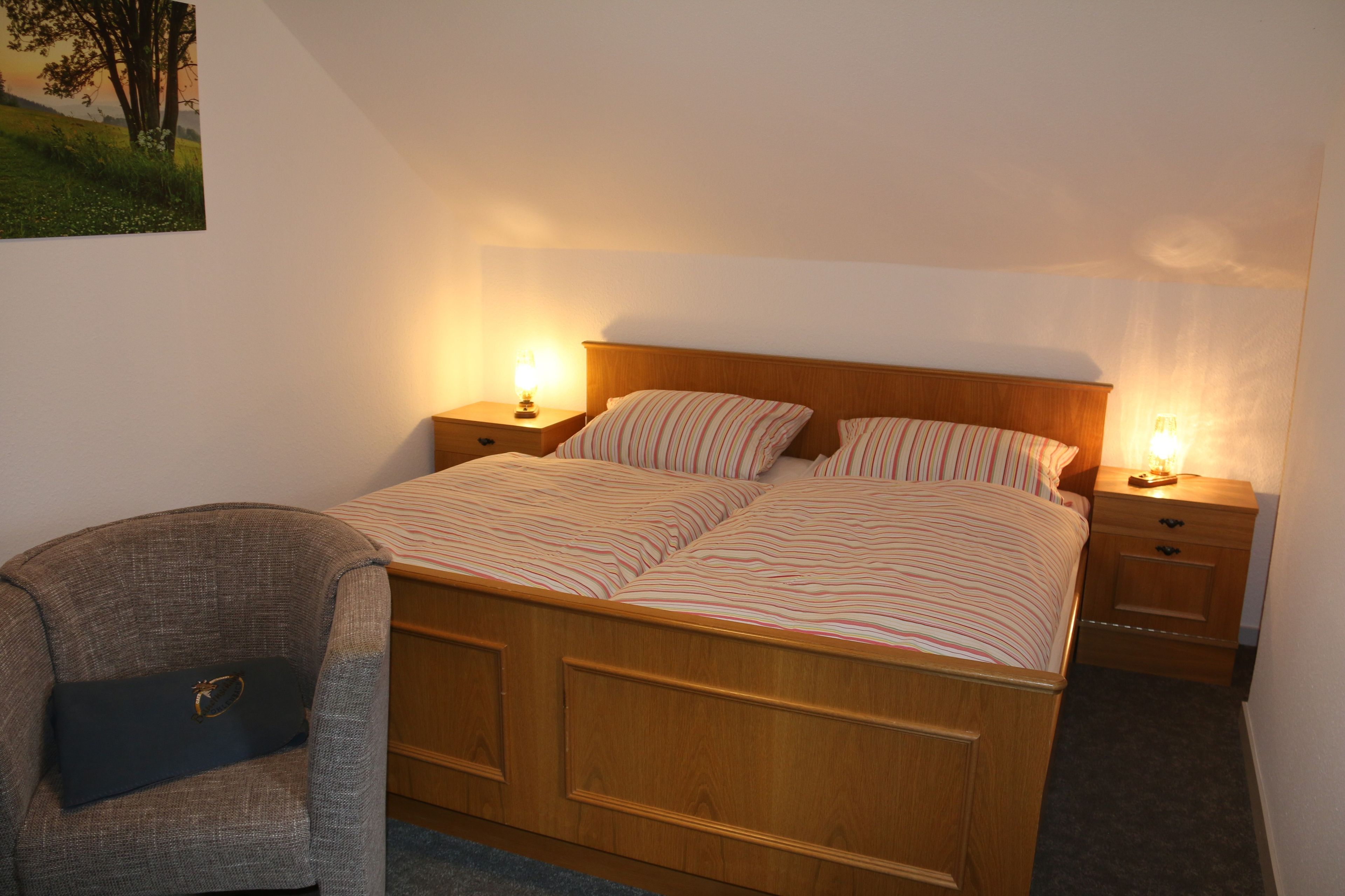 Ein Schlafzimmer mit einem hölzernen Bett, zwei Nachttischen mit Lampen, einem Sessel und einem Bild an der Wand.
