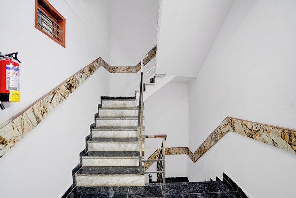 A staircase with marble steps and handrails, a fire extinguisher on the wall, and a wooden window frame.