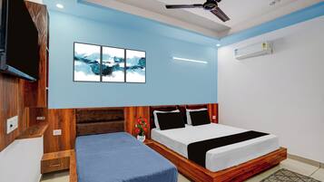 Ein Hotelzimmer mit einem Bett, einem Nachttisch, einem an der Wand befestigten Fernseher, einem Deckenventilator und einer Wandklimaanlage.