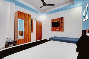 A modern bedroom with a bed, a ceiling fan, a TV mounted on a wooden panel, and a bedside table with a kettle and cups.