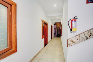 A hallway with a fire extinguisher mounted on the wall, wooden doors, and a tiled floor.