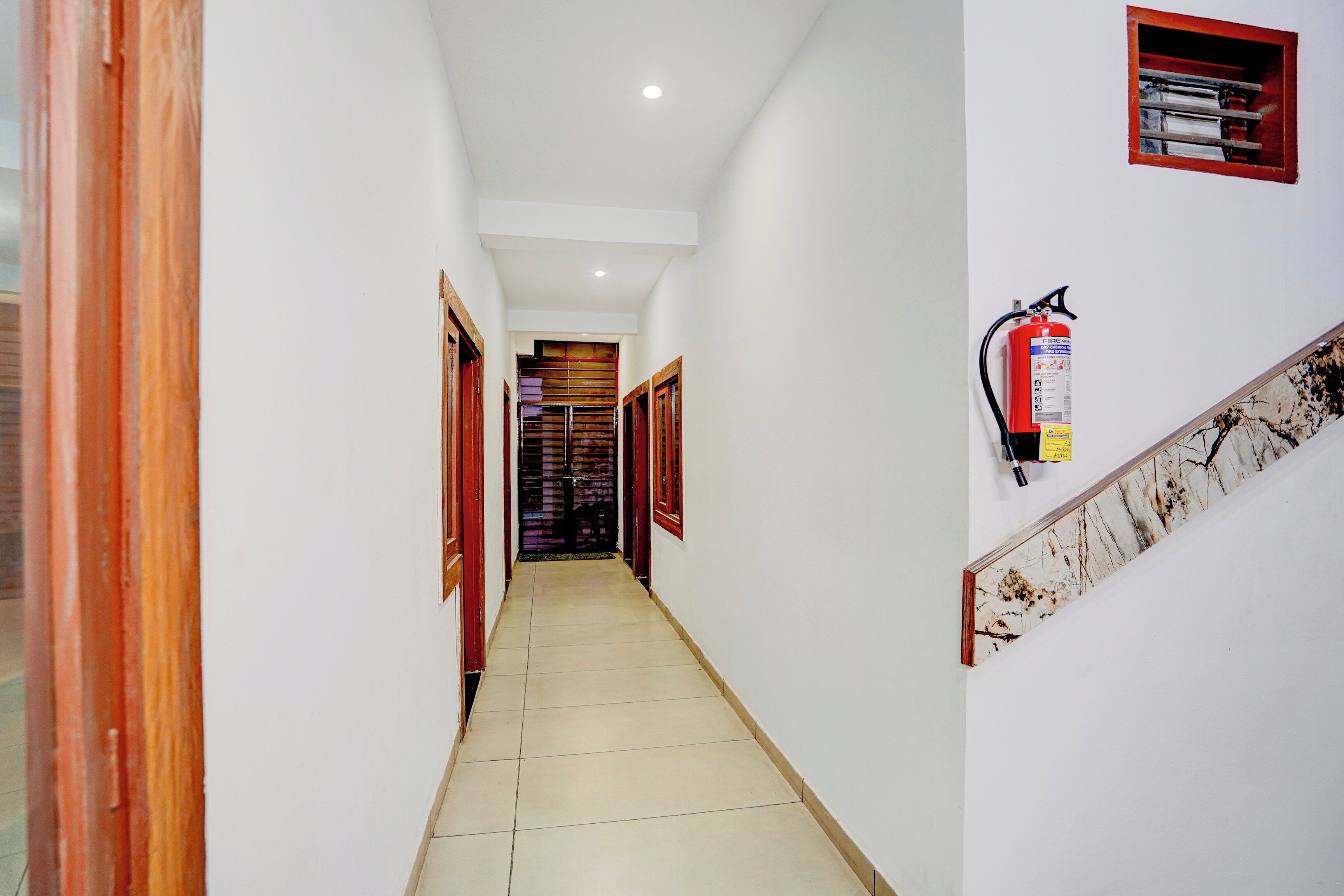 Un pasillo con un extintor en la pared, suelo de baldosas y puertas de madera a ambos lados.