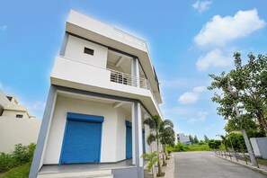 A modern two-story building with a flat roof, a balcony on the upper floor, and a gated entrance.