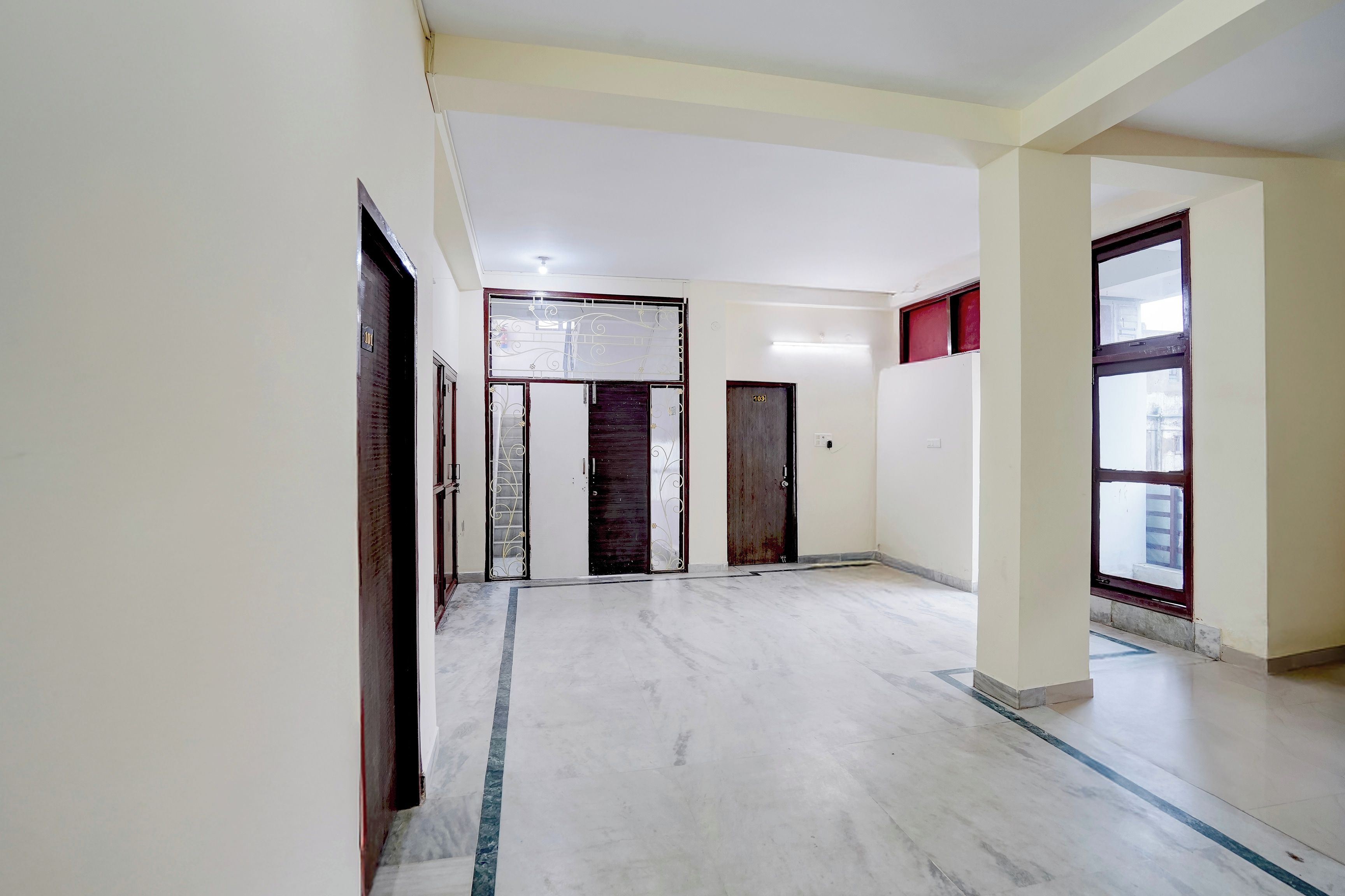 Un pasillo con piso de mármol, una puerta de madera con reja de metal y una ventana con marco rojo.