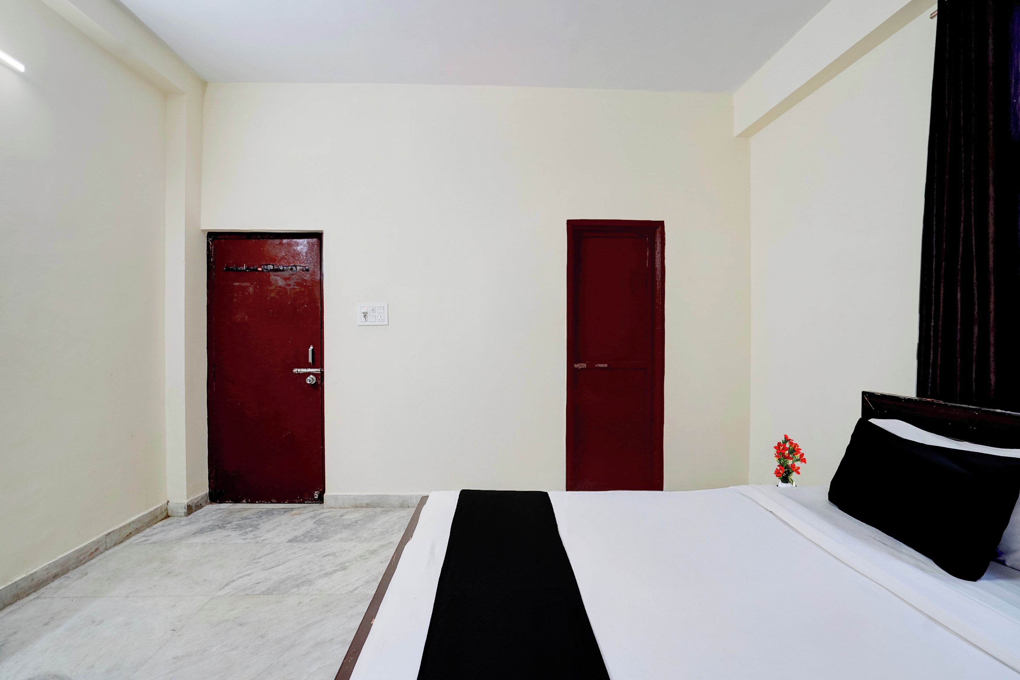 A hotel room with a bed, two doors, a small table with a vase, and a marble floor.