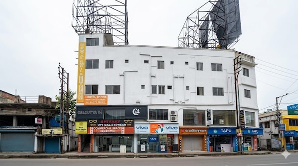 A multi-story building with commercial spaces on the ground floor, including optical stores and a restaurant. - Hotel Royal Empire (Barasat)