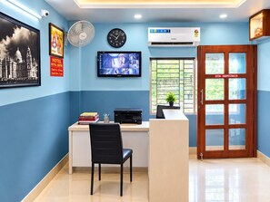 A reception area with a desk, chair, clock, television, and a door with a window. - Hotel Royal Empire (Barasat)