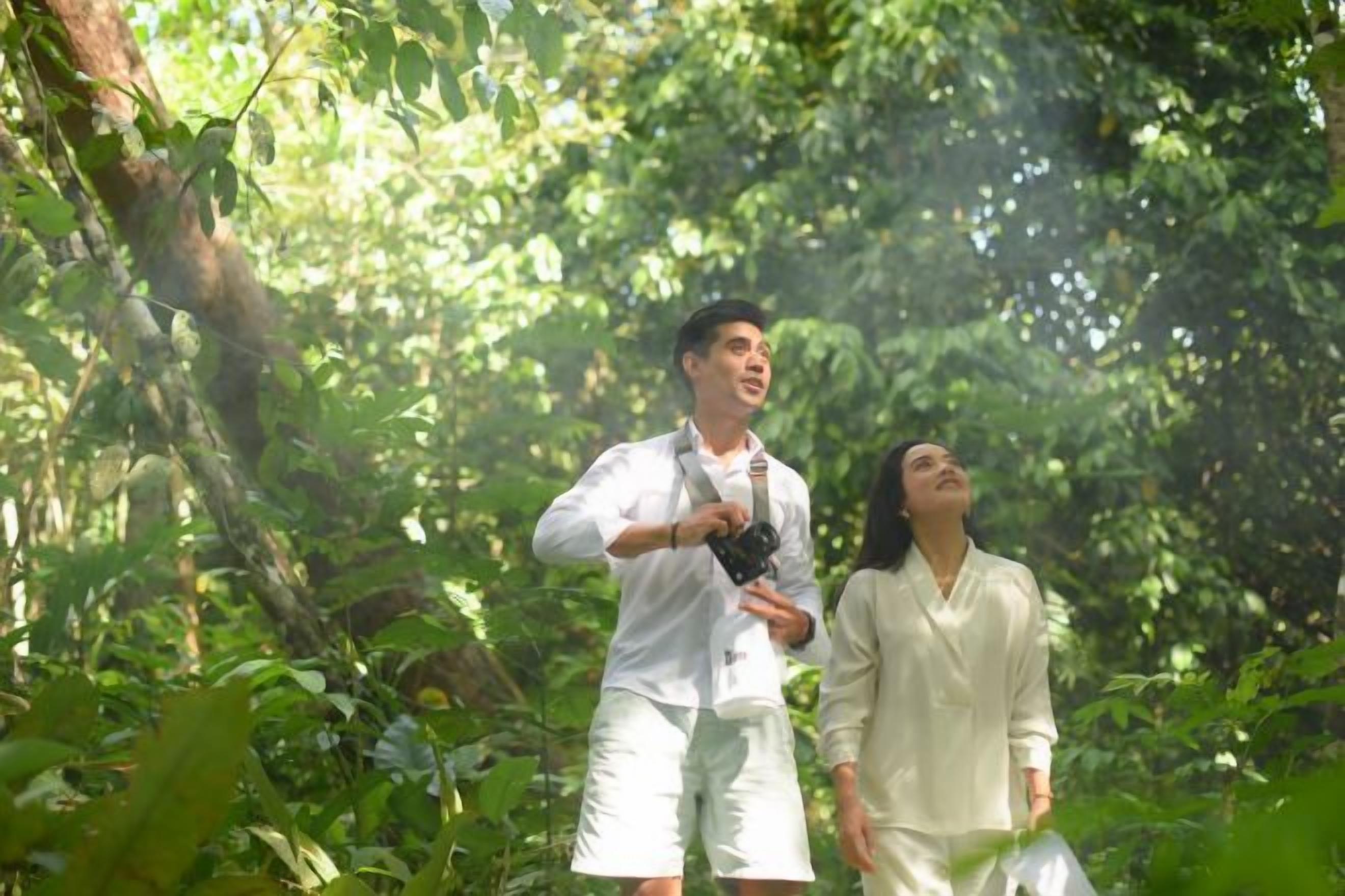 Two individuals in a forested area, one holding a camera.