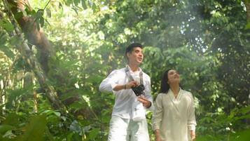 Two individuals in a forested area, one holding a camera.
