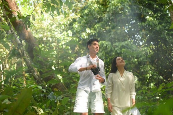 Two individuals in a forested area, one holding a camera.