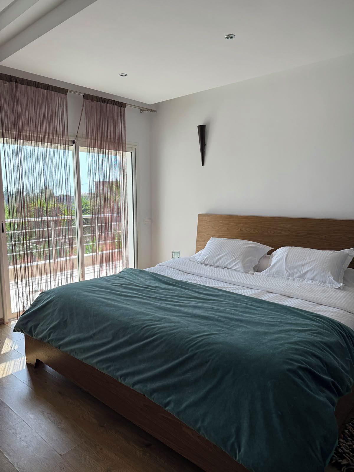 Une chambre avec un grand lit, une tête de lit en bois et une vue sur l’extérieur, accessible par une porte coulissante.
