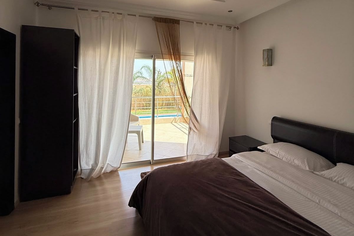 A bedroom with a bed, a wardrobe, and a view of a pool through a glass door.