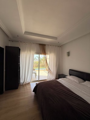A bedroom with a bed, a wardrobe, and a view of a pool through a glass door. - VINEA HOUSE  (Skhirat)