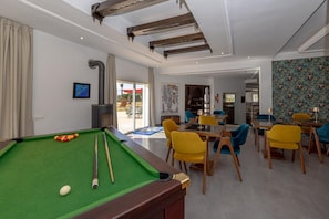 A pool table with a green felt surface, a cue stick, and billiard balls. There is a dining area with yellow chairs and a table. The room has white walls and a ceiling with exposed beams. - VINEA HOUSE  (Skhirat)