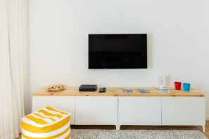 A modern living room with a flat-screen TV mounted on the wall, a wooden console table with a bowl of snacks, a remote control, and a welcome sign. - Apartment 'Light Filled' with Terrace (Porto)