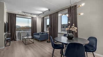 En moderne stue med sofa, spisebord med stole, fjernsyn og et stort vindue med gardiner.