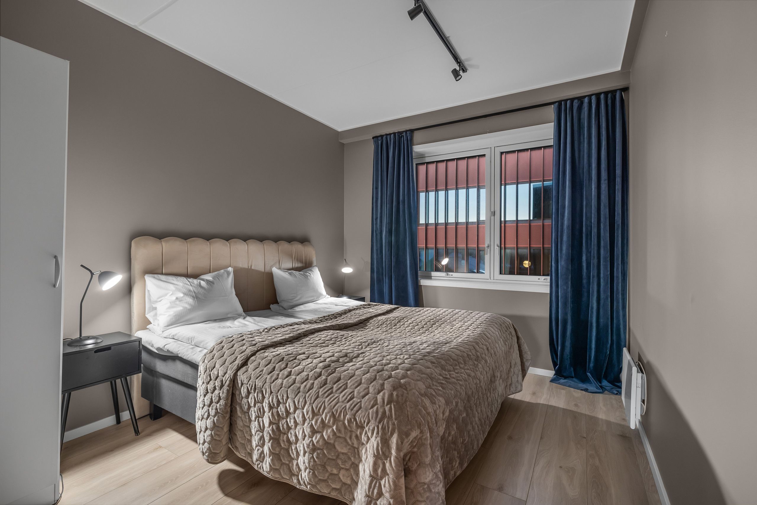 Un dormitorio con cama, mesita de noche, lámpara y ventana con cortinas.
