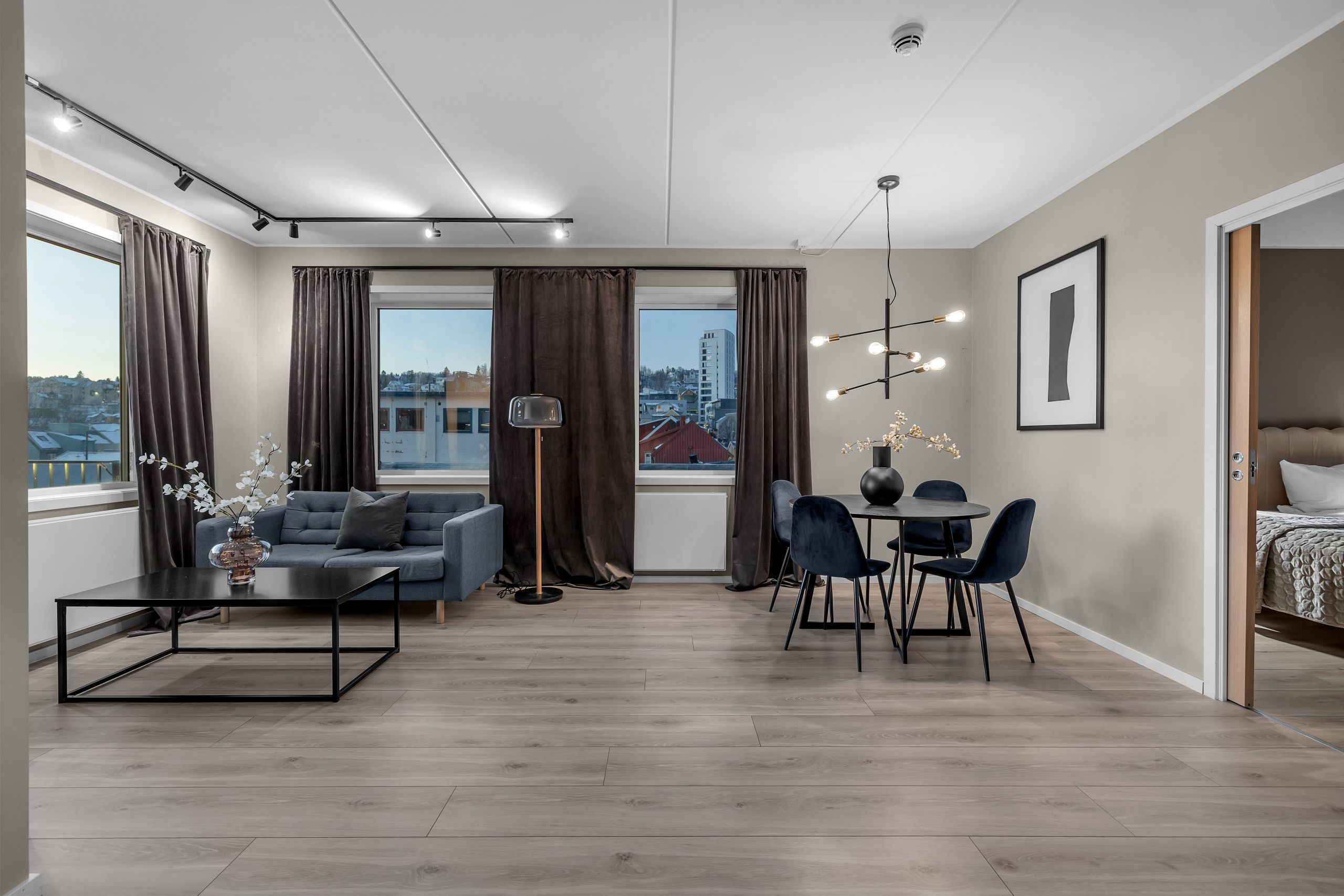 Un salon moderne comprenant un canapé, une table basse, une table à manger avec des chaises, et offrant une vue sur la ville grâce à de grandes fenêtres.