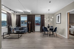 Ein modernes Wohnzimmer mit Sofa, Couchtisch, Esstisch mit Stühlen und Blick auf die Stadt durch große Fenster.