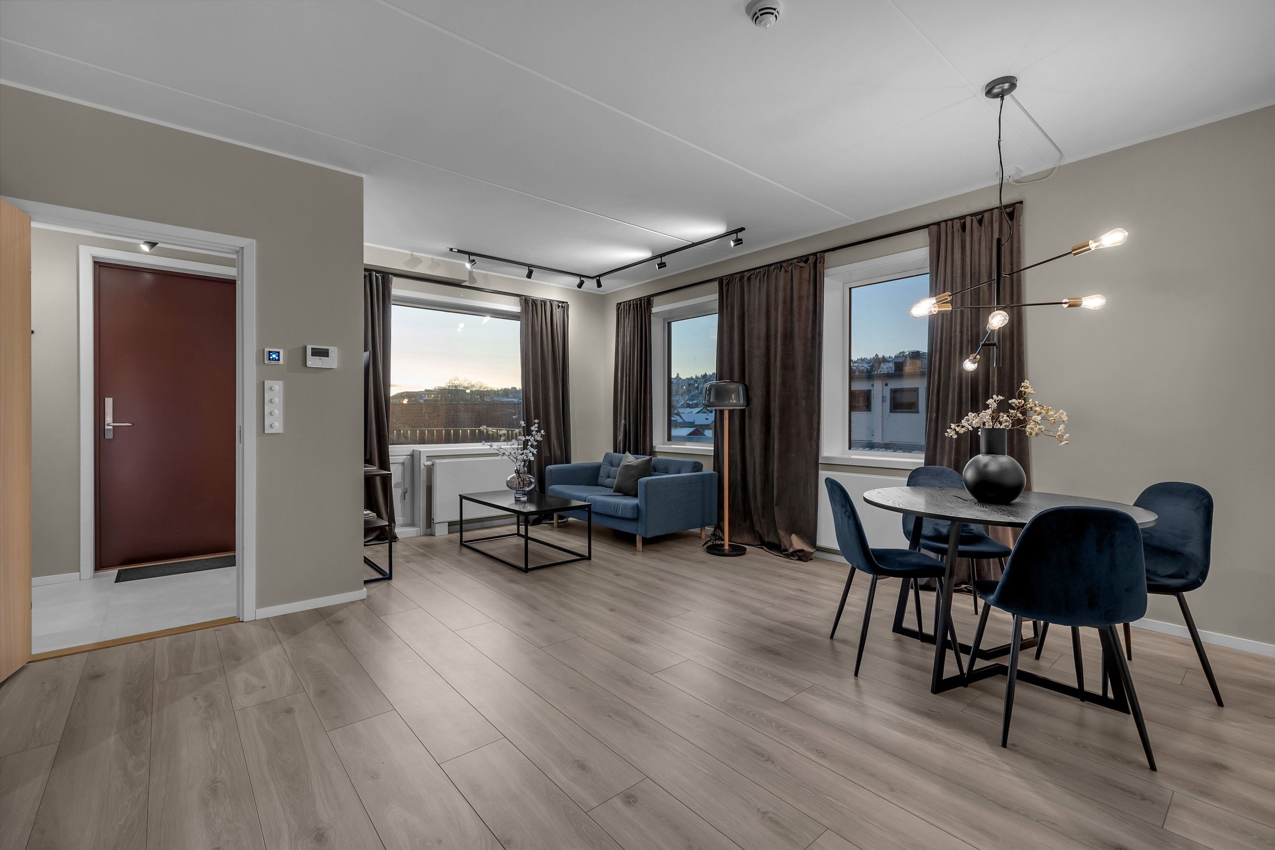 Un salon moderne comprenant un canapé, une table à manger avec des chaises, une grande fenêtre avec des rideaux et un luminaire au plafond.