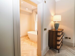 Ein Badezimmer mit einer freistehenden Badewanne, einem Holzwaschtisch mit einer Lampe und einem Fischgrätenboden.