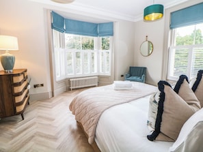 Ein Schlafzimmer mit Bett, Stuhl, Kommode, Fenster mit Rollläden und Heizkörper.