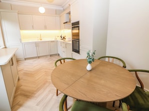 Eine moderne Küche mit weißen Schränken, einem Holztisch und einer Vase mit grünen Blättern.