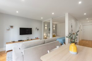 Ein modernes Wohnzimmer mit einer Couch, einem Esstisch, einem an der Wand befestigten Fernseher und einem Spiegel, der den Raum widerspiegelt.