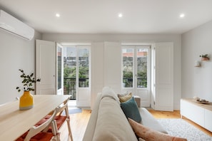 A modern living room with a sofa, a dining table with chairs, and a balcony with a view of the city. - Apartment 'Almada Prime with Balcony' (Porto)