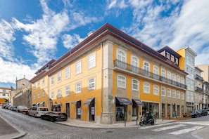 Ein gelbes Gebäude mit vielen Fenstern und einem roten Dach, das an einer Kopfsteinpflasterstraße steht.