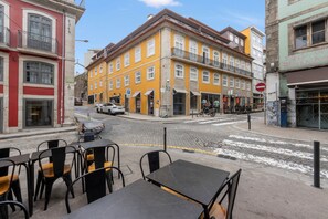 A street view with a yellow building, parked cars, and outdoor seating with tables and chairs. - Apartment 'Cosy and Charming Almada Prime' (Porto)