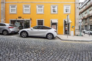 A street view with a yellow building, a white car parked in front, and cobblestone pavement. - Apartment 'Cosy and Charming Almada Prime' (Porto)