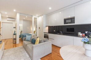A modern apartment with a grey sofa, a dining table, and a kitchen with a microwave. - Apartment 'Cosy and Charming Almada Prime' (Porto)