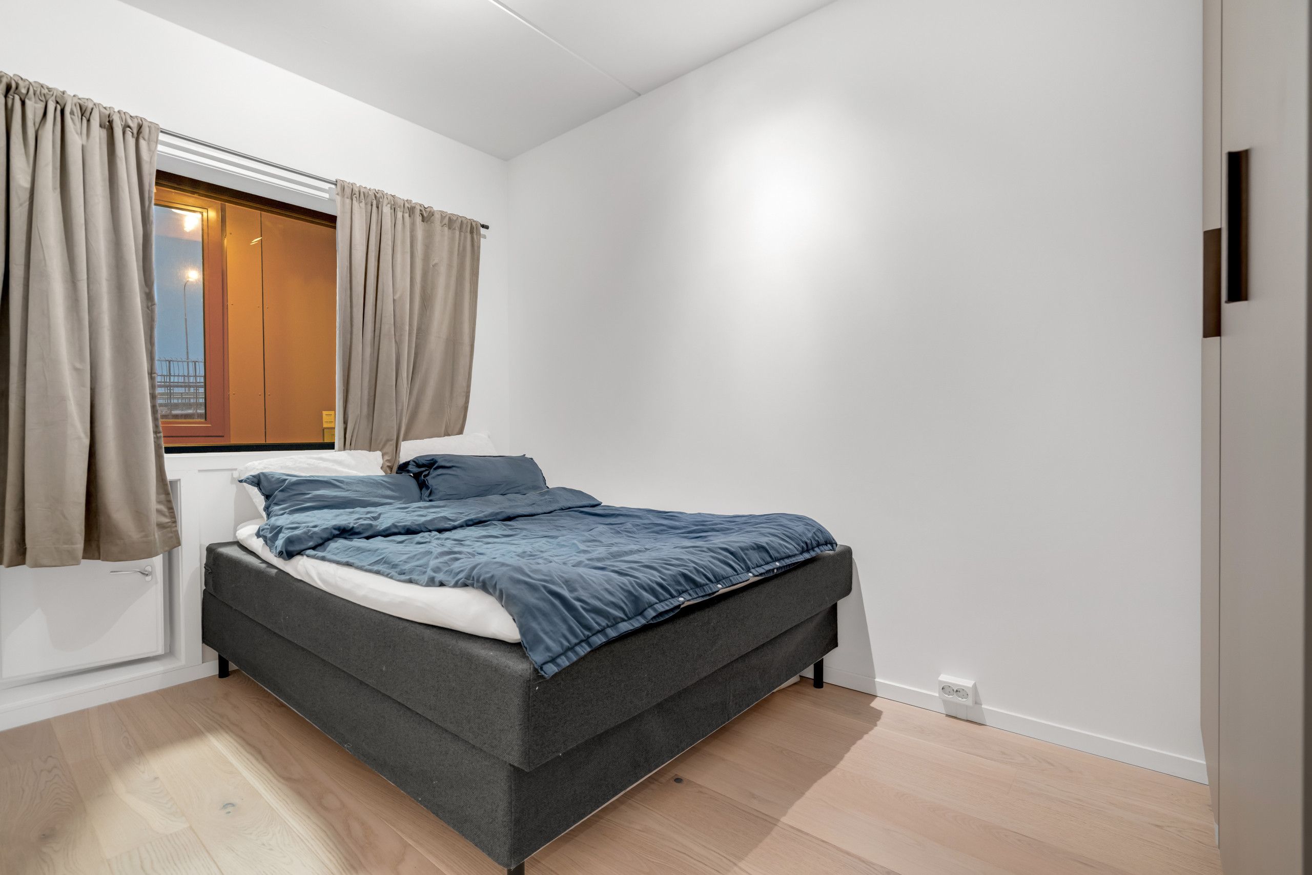 A bedroom with a bed, curtains, a window, and a door.