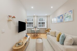 A modern living room with a flat-screen TV, a dining area with a table and chairs, and a sofa with cushions. - Apartment 'Enchanting Almada Prime' (Porto)