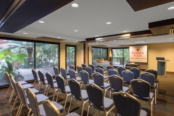 Un salón de conferencias con filas de sillas, un atril y una pantalla para presentaciones.
