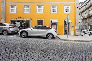Straßenansicht mit einem gelben Gebäude, einem davor geparkten weißen Auto und Pflastersteinpflaster.