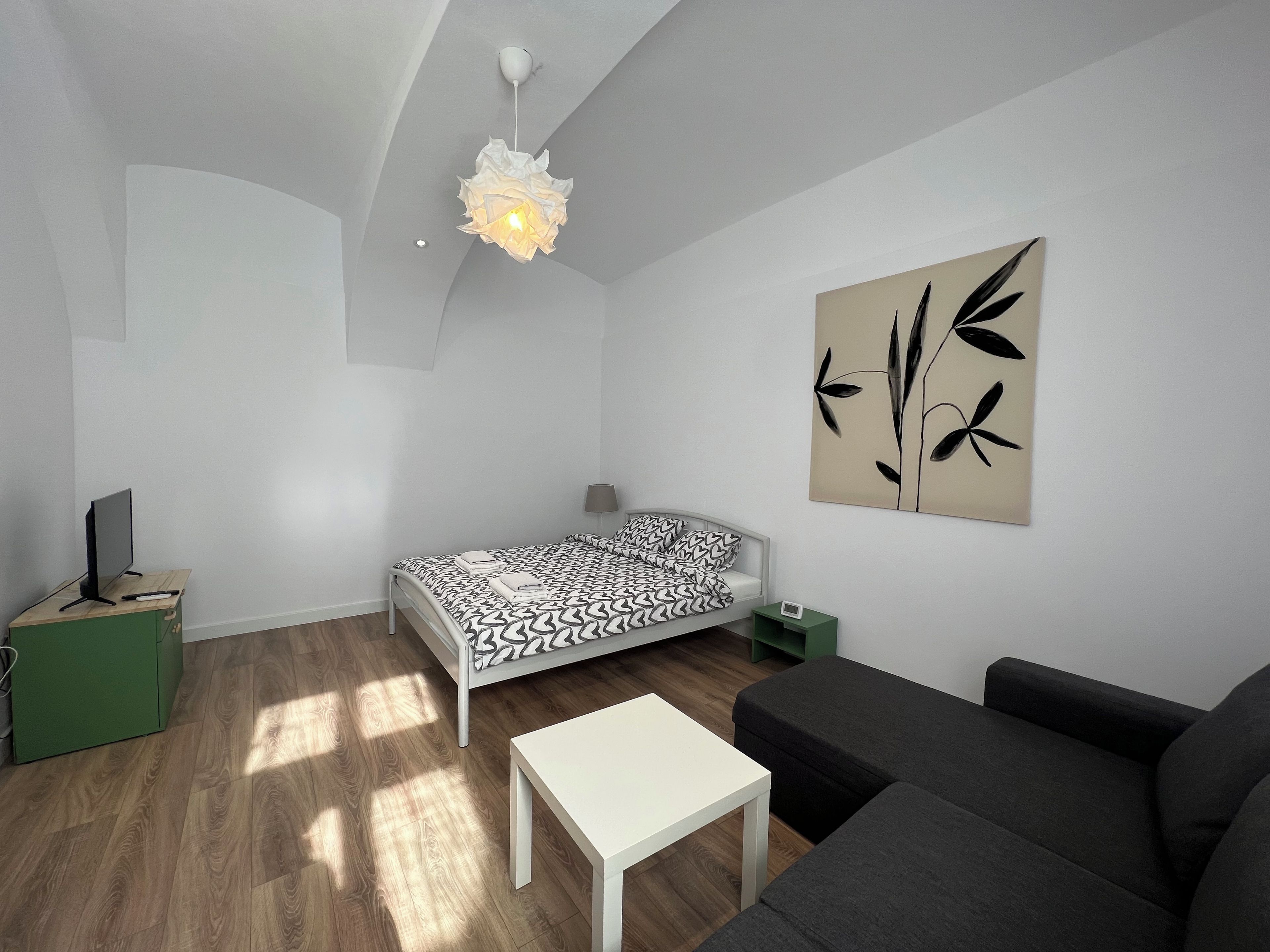 Ein modernes, minimalistisches Wohnzimmer mit einem Bett, einer Couch, einem kleinen Tisch und einem Wandbild.