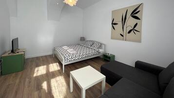 Ein modernes, minimalistisches Wohnzimmer mit einem Bett, einer Couch, einem kleinen Tisch und einem Wandbild.