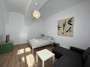 A modern, minimalist living room with a bed, a sofa, a small table, and a wall-mounted artwork. - Your Cosy Home in Medieval Brasov (Brașov)