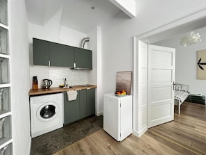 Uma cozinha compacta com máquina de lavar, um frigorífico pequeno e um espaço de refeições com mesa e cadeiras.
