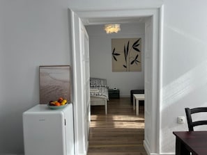 Corredor que dá para um quarto com cama, mesa de cabeceira e uma obra de arte na parede.