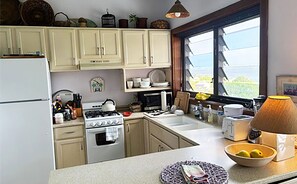 A kitchen with a refrigerator, stove, oven, microwave, sink, and various kitchen utensils. There is a window with a view of the outdoors. - Blue Seas 11E Lavender Hill: Ocean Views, Pool & Walk-to-Town Location (St. John)
