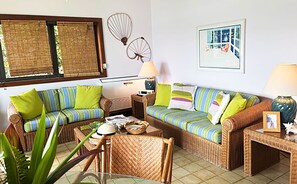 A room with wicker furniture, a dining table, and a window with blinds. - Blue Seas 11E Lavender Hill: Ocean Views, Pool & Walk-to-Town Location (St. John)
