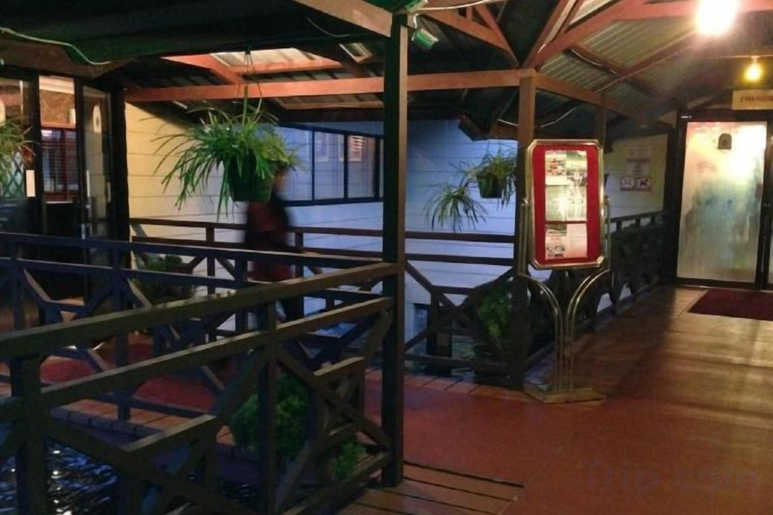 Un espacio al aire libre techado con baranda de madera, plantas en macetas y un letrero informativo rojo.