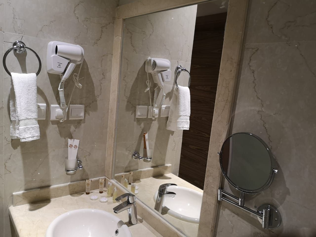 A bathroom with two sinks, a large mirror, and two hair dryers mounted on the wall.