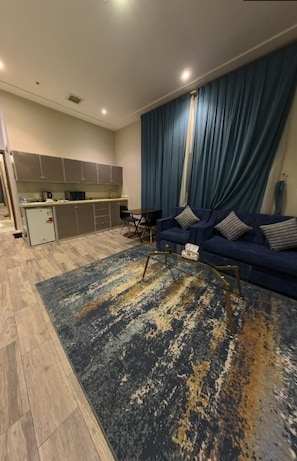 Una sala de estar con sofá, mesa de centro y un área de cocina con armarios y refrigerador.